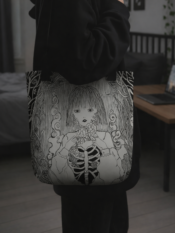 Person holding a tote bag with a black and white illustration of a skeleton girl.